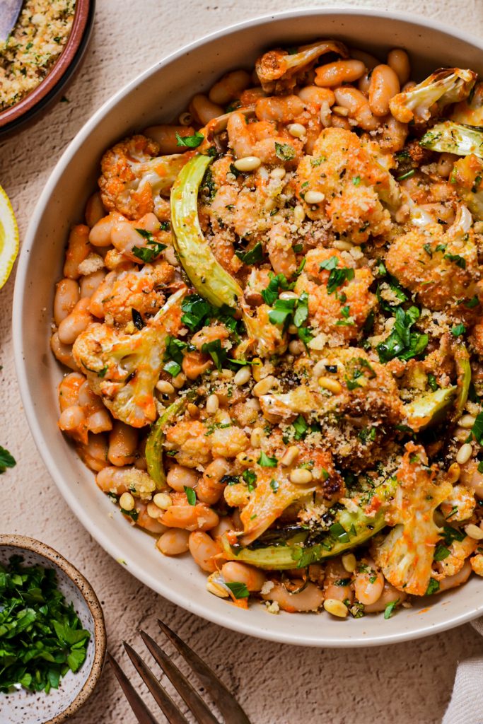 Close up shot of roasted cauliflower and cannellini beans coated in a red pepper sauce.