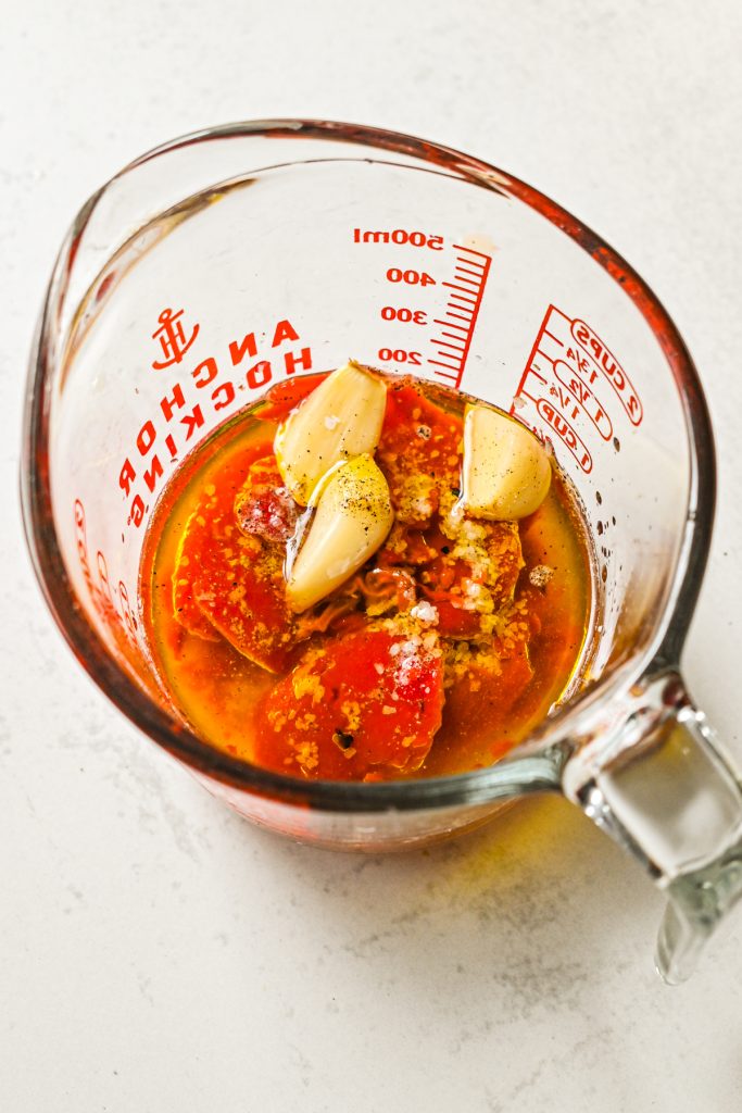 Ingredients needed for red pepper sauce in a measuring cup.