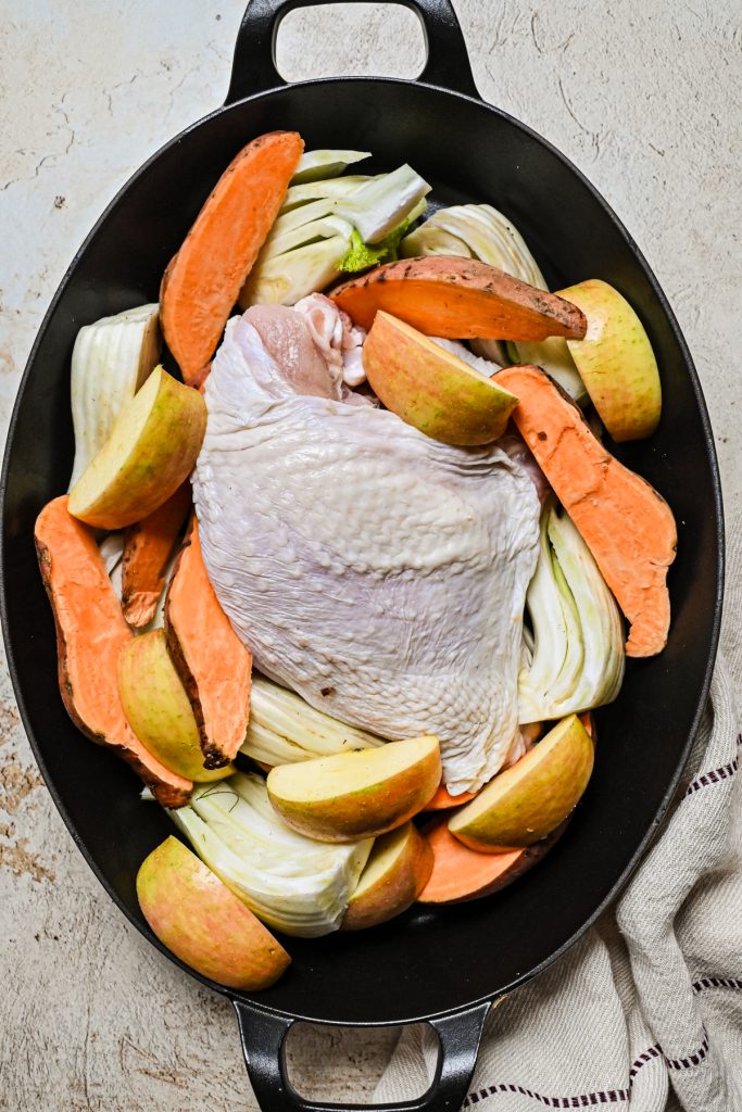 Turkey breast in a roasting pan with sweet potatoes, fennel and apples before being cooked.