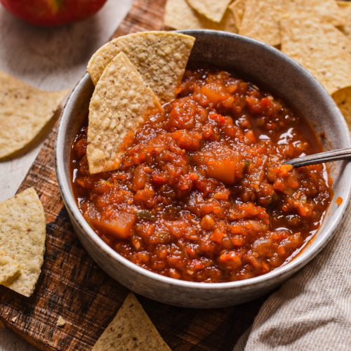 Souther apple salsa served in a bowl with a spoon and tortilla chips.