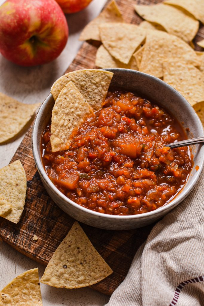 Souther apple salsa served in a bowl with a spoon and tortilla chips.