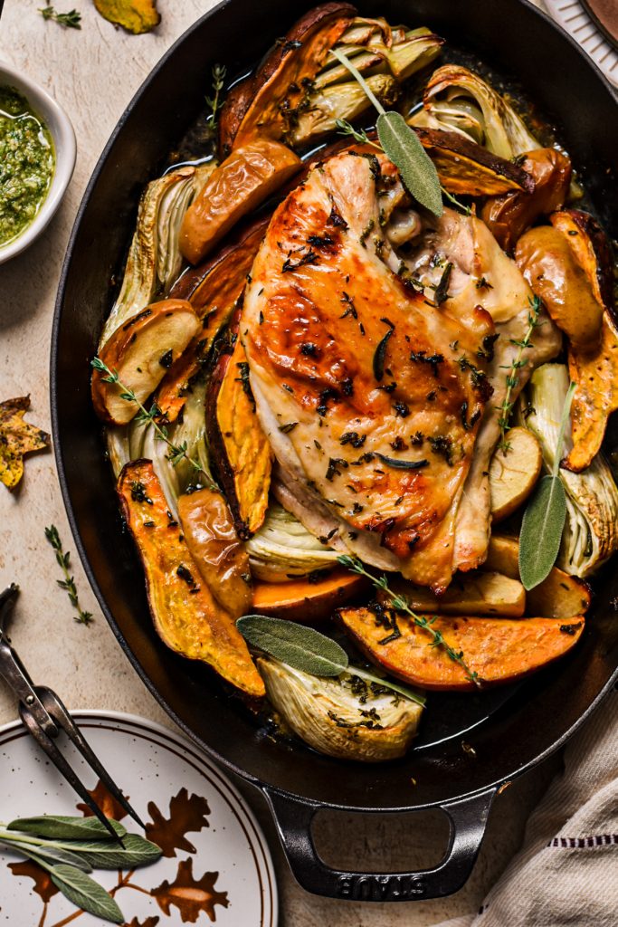 Maple roasted turkey breast in a roasting pan with roasted vegetables around it and fresh herbs on top.