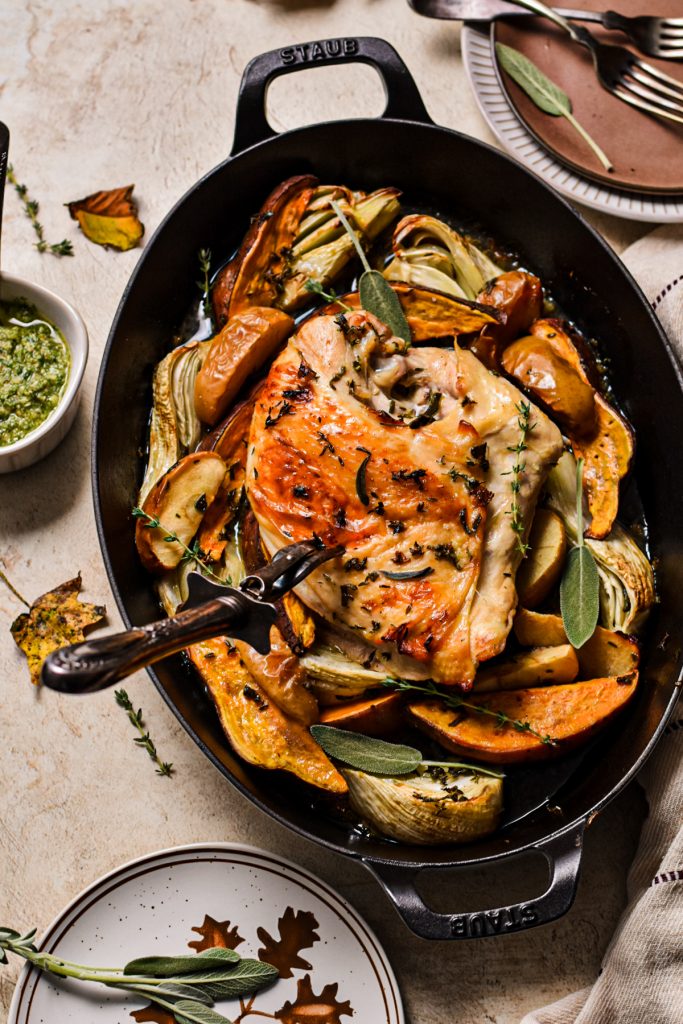 Maple roasted turkey breast with a carving knife in it sitting on a bed of vegetables.