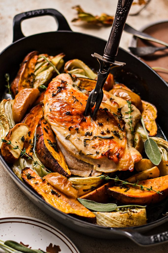 Carving fork inserted into the turkey breast with a bed of vegetables around it.