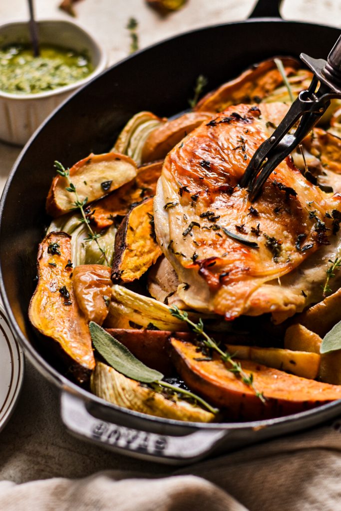 Carving fork in a roasted turkey breast while it is in the roasting pan with vegetables.