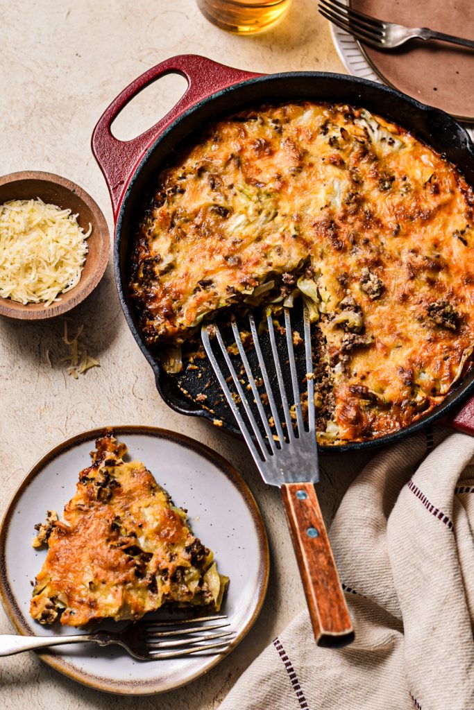 Beef and cabbage gratin in a skillet with some of it served on a plate.