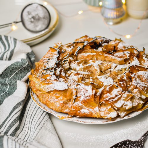 Apple tart on a plate with some Christmas decorations in the background.