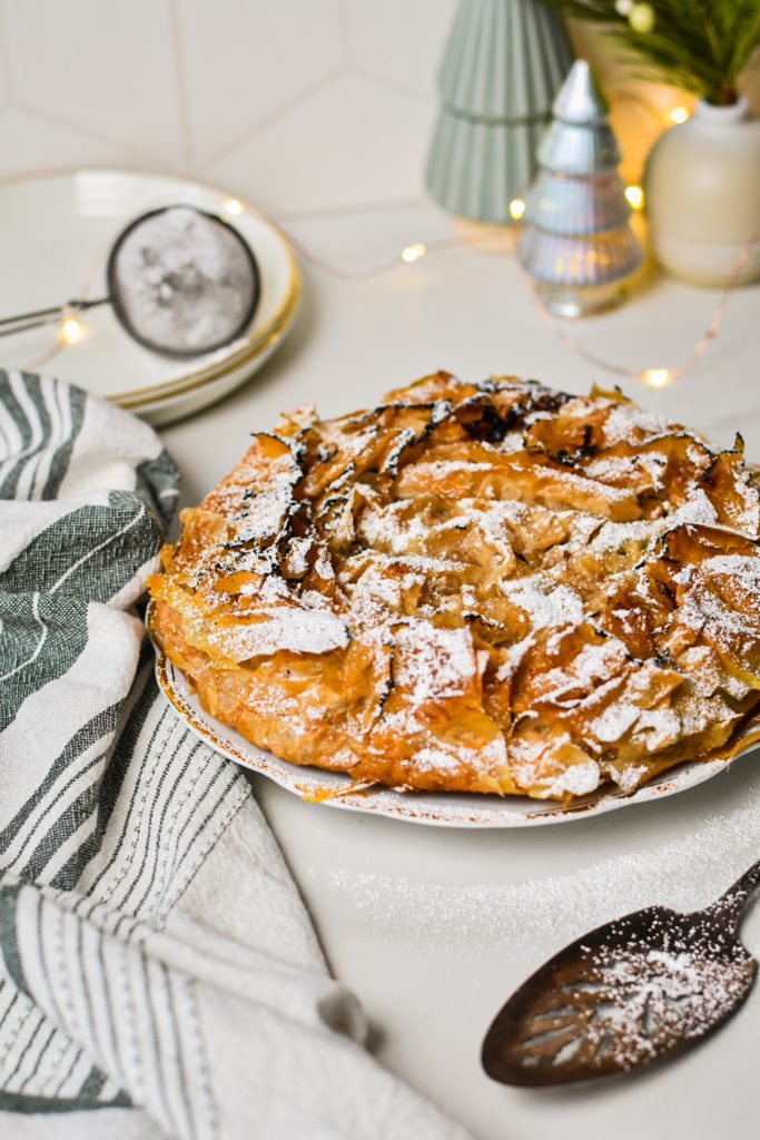 Apple tart on a plate with some Christmas decorations in the background.
