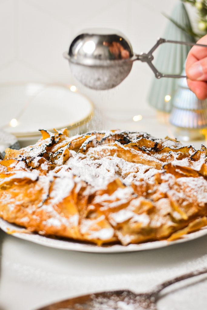 Dusting the flaky apple tart with powdered sugar.
