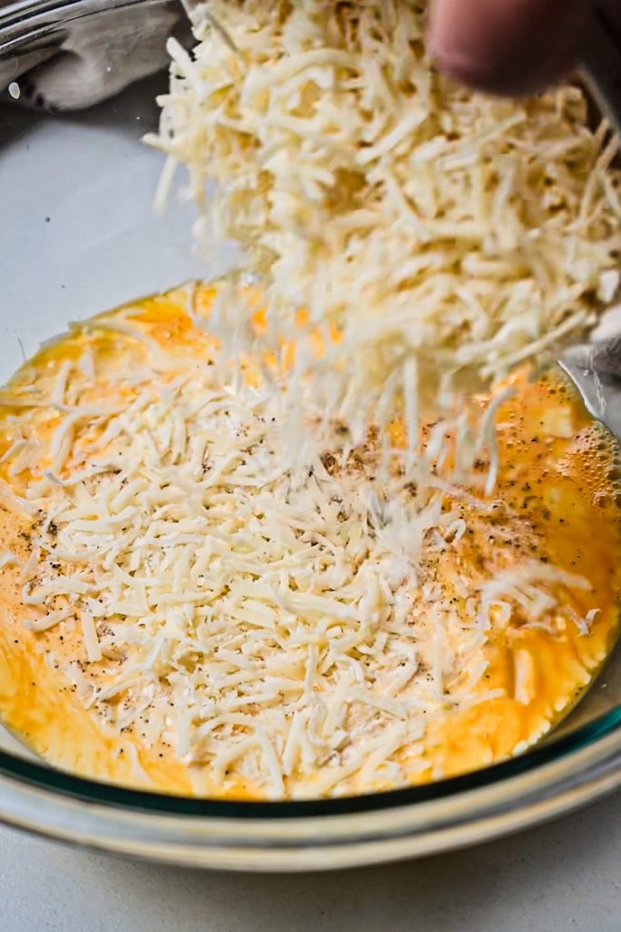 Eggs, salt and pepper, heavy cream, and parmesan cheese being mixed together in a mixing bowl.