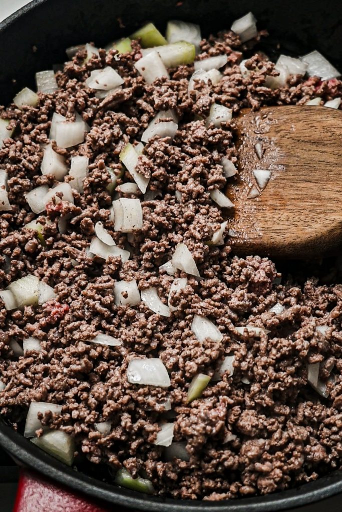 Mixing together chopped onions and ground beef in a skillet with a wooden spoon.