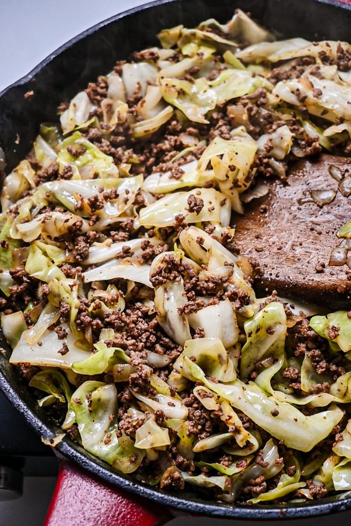 Chopped cabbage added to the ground beef mixture in a skillet.