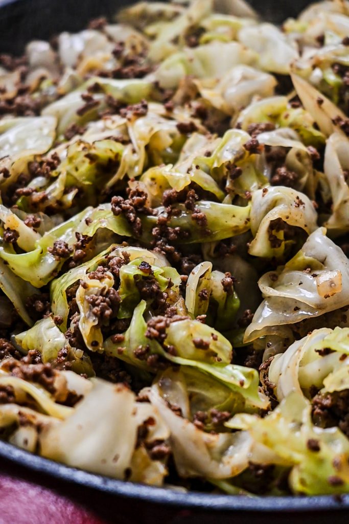 Cabbage and ground beef mixture in a cast iron skillet being cooked.
