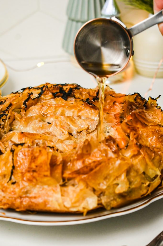 Pouring cognac over the top of the baked flaky apple tart.