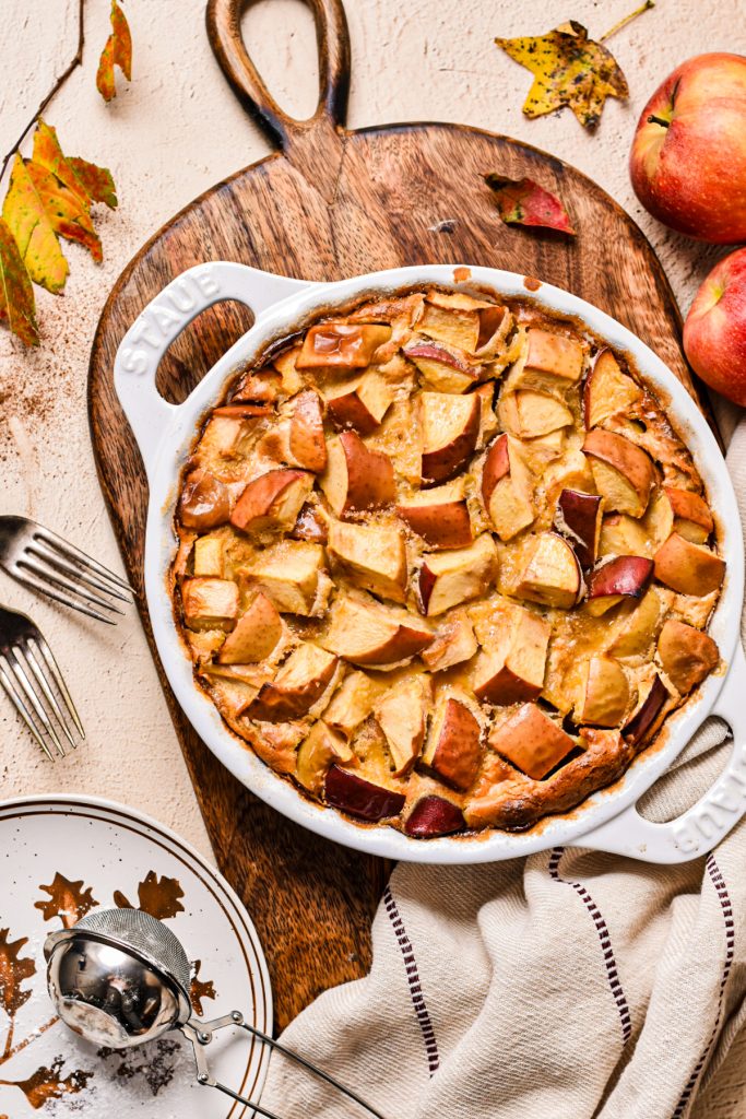Overhead shot of an apple flaugnarde in a white pie dish on a wooden board.