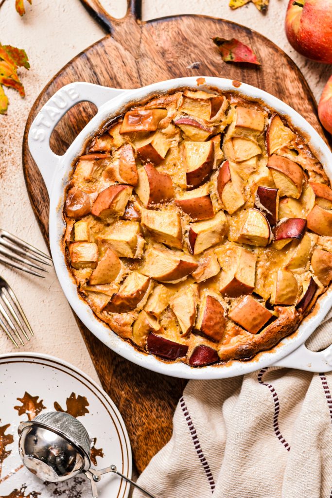 Apple flaugnarde in a white pie dish on a wooden board.