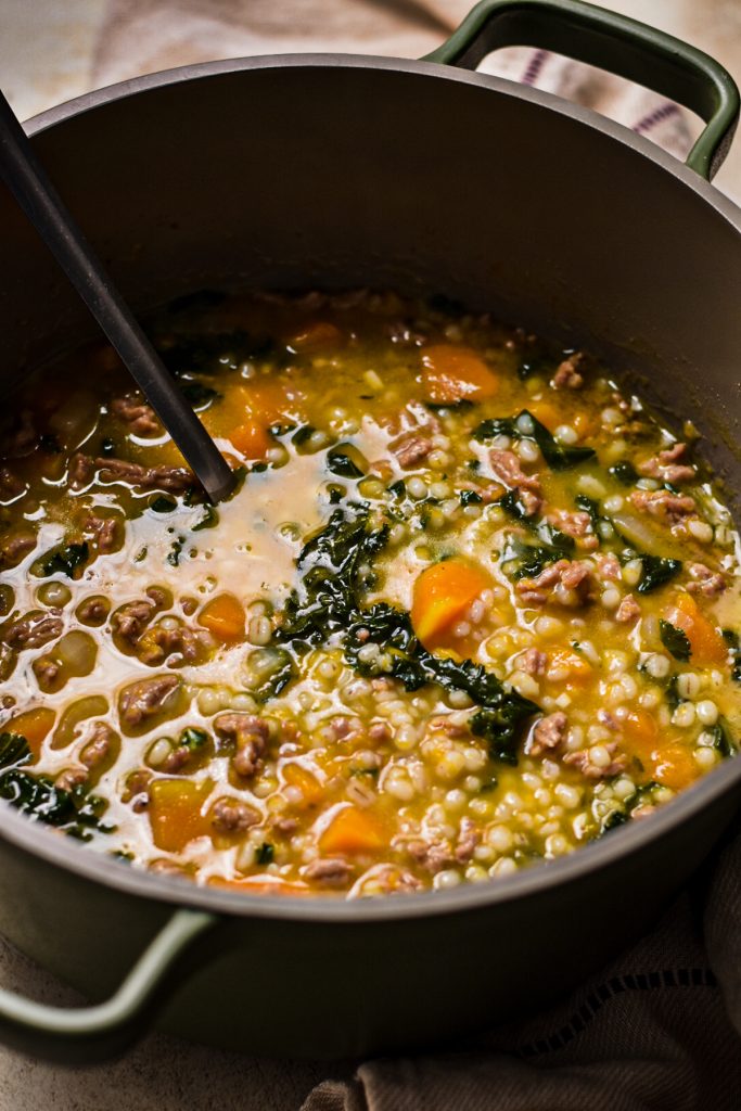 Large pot full of butternut squash, sausage, kale and barley soup.