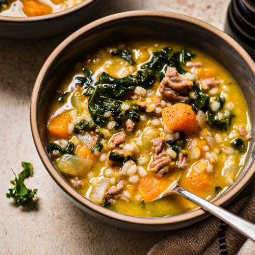 Bowl of butternut squash, sausage, kale and barley soup with another bowl behind it.