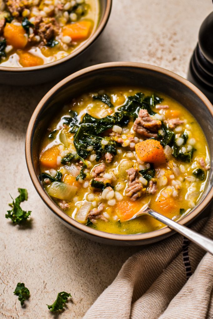 Bowl of butternut squash, sausage, kale and barley soup with another bowl behind it.