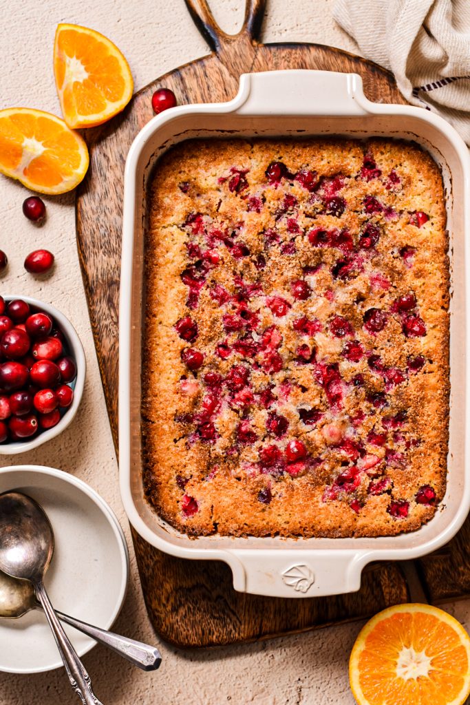 Overhead shot of cornmeal orange cranberry cobbler in a white baking dish on a wooden board.