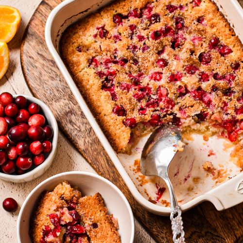 Cranberry orange cobbler in a white baking dish with a serving in a bowl on the side.