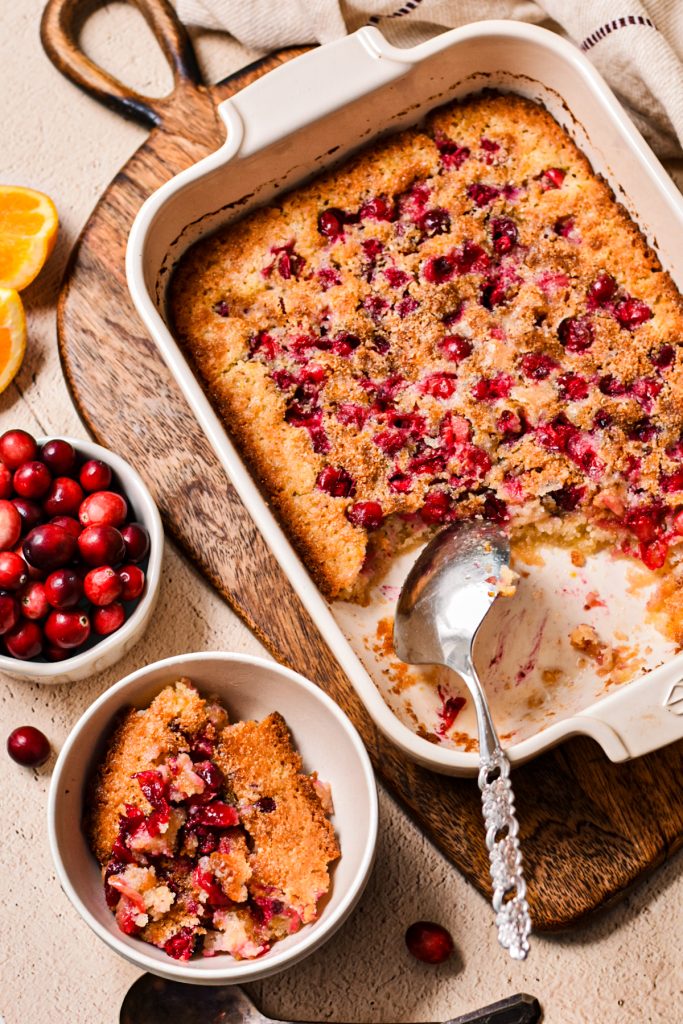 Cranberry orange cobbler in a white baking dish with a serving in a bowl on the side.