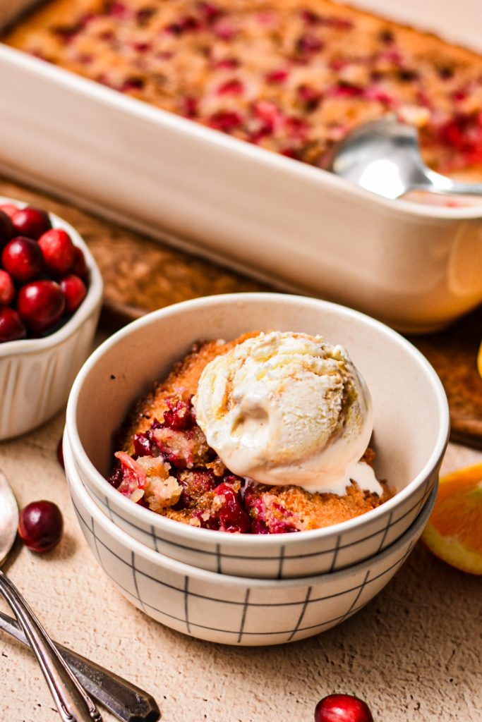 Serving of cranberry orange cobbler in a bowl with a scoop of ice cream on top.
