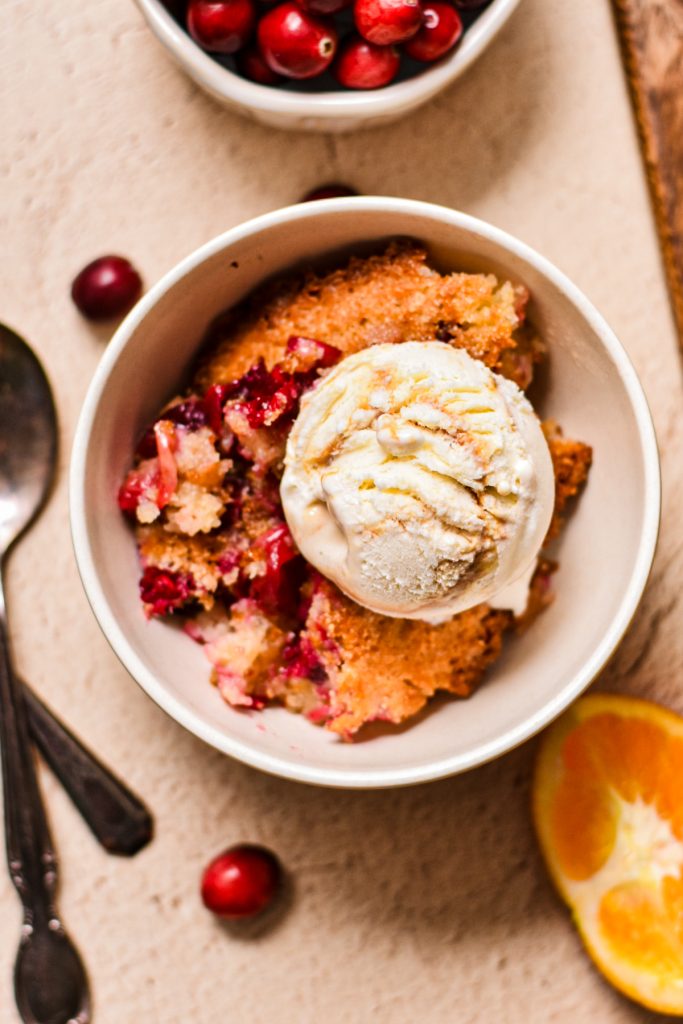Cornmeal orange cranberry cobbler in a bowl with a scoop of ice cream on top.
