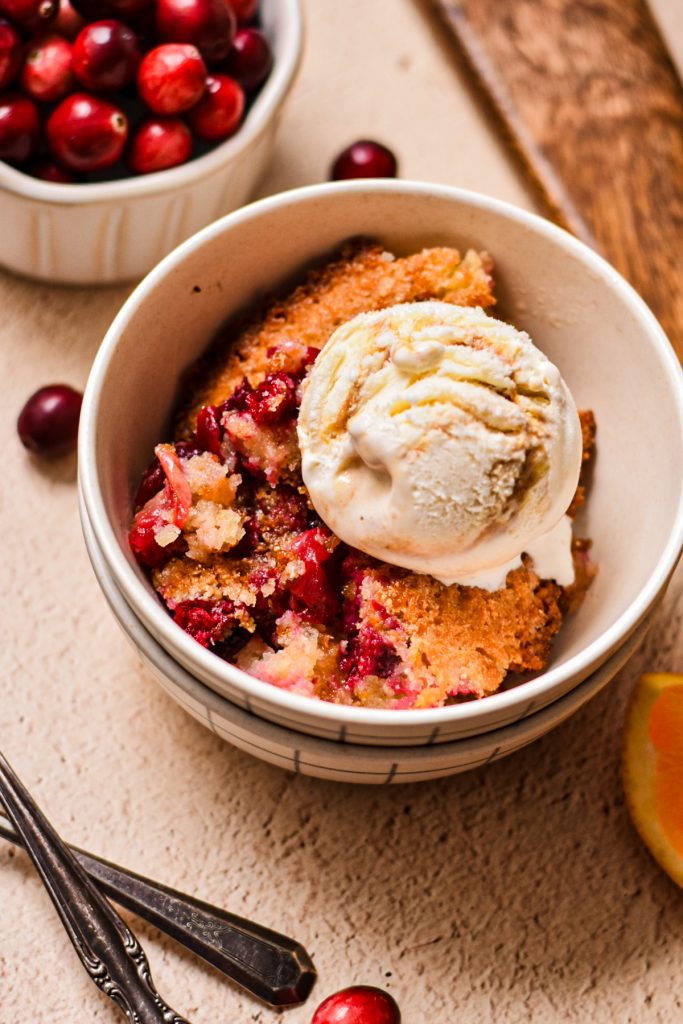 Serving of cornmeal orange cranberry cobbler in a bowl with a scoop of vanilla ice cream.