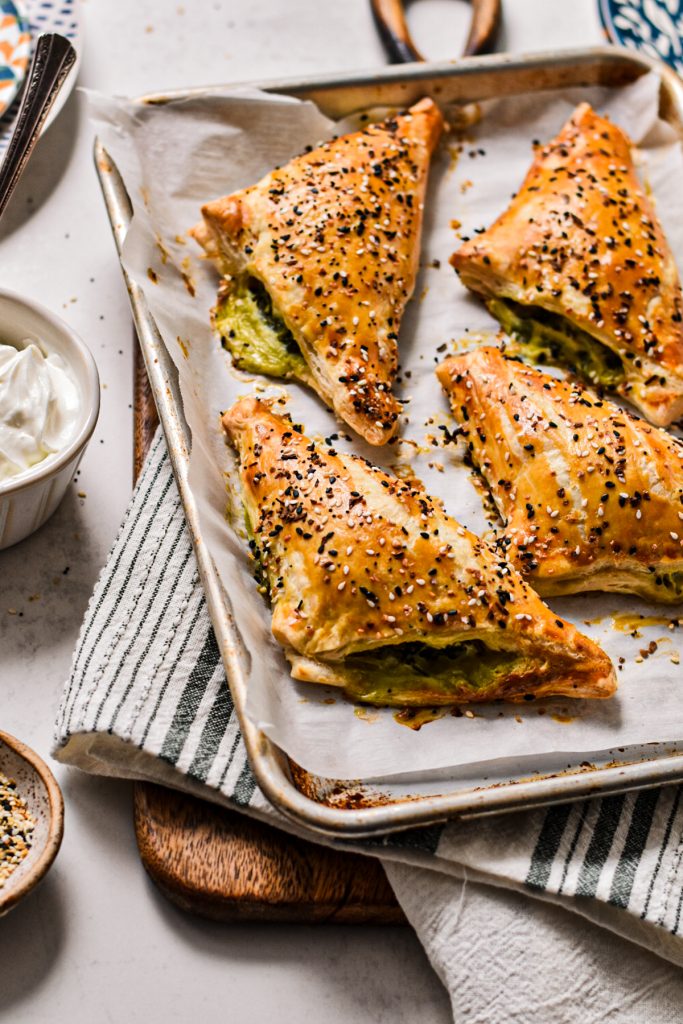 Four spanakopita turnovers on a sheet pan set on a wooden board.
