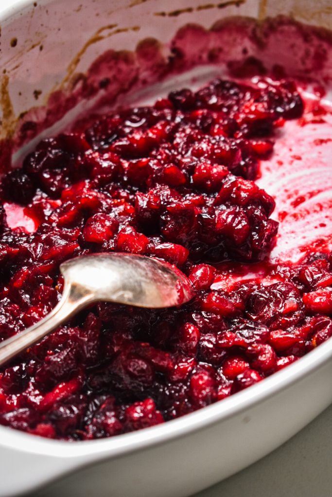 Roasted cranberry sauce in a baking dish with a spoon stirring it.