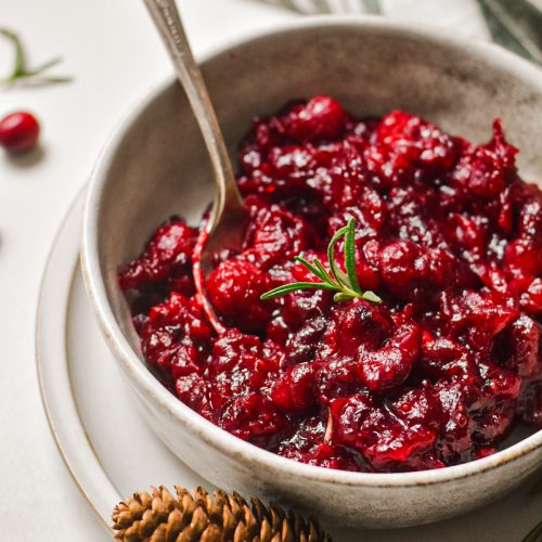 Ginger balsamic roasted cranberry sauce served in a serving bowl with a pinecone next to it.