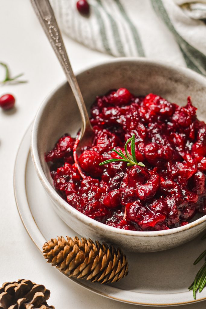 Ginger balsamic roasted cranberry sauce served in a serving bowl with a pinecone next to it.