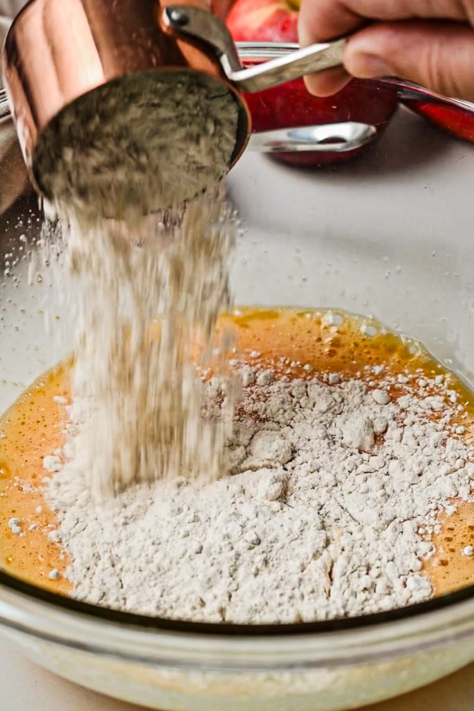 Adding flour to the egg and sugar mixture in a glass mixing bowl.