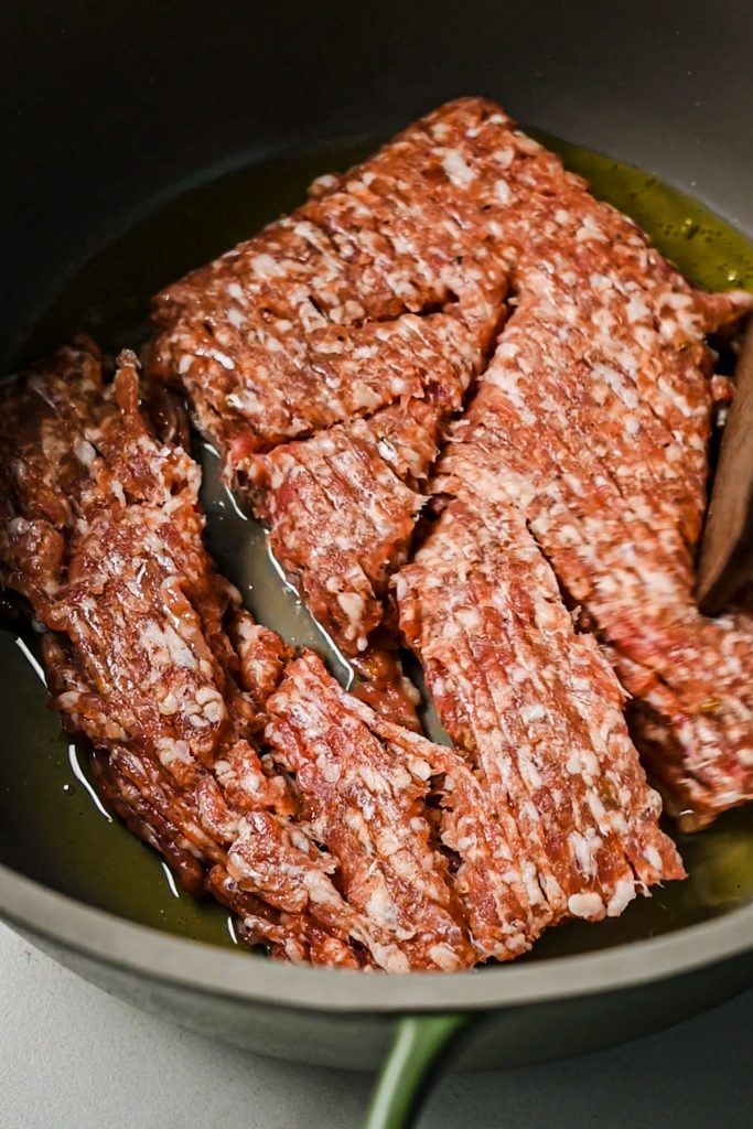 Italian sausage being cooked in the bottom of a pot with olive oil.