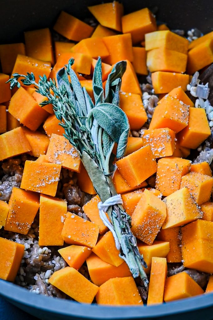Butternut squash and a bundle of fresh herbs added to the pot.