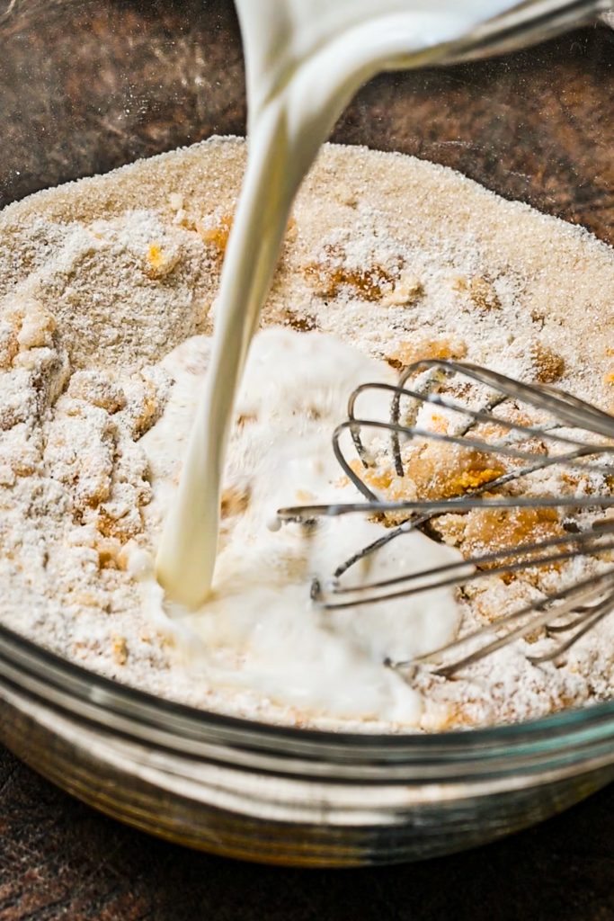 Pouring the milk into the cobbler batter in a glass mixing bowl.