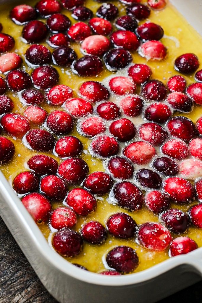 Fresh cranberries on top of the cornmeal cobbler batter and sugar being sprinkled on top.