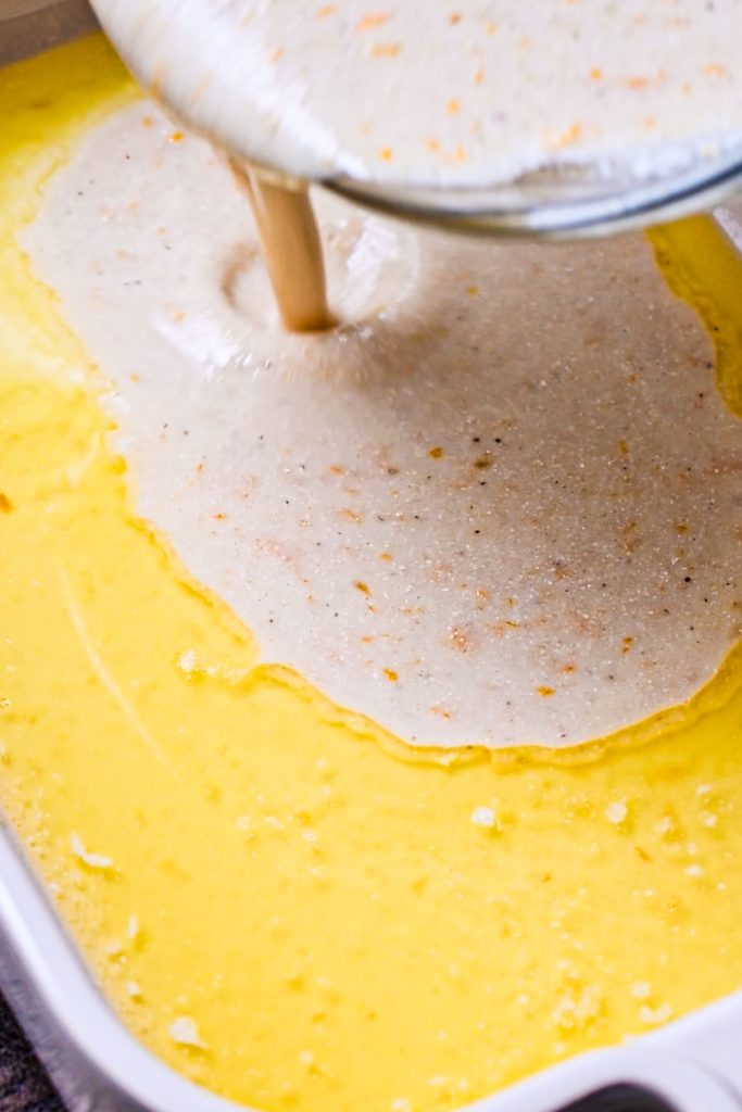 Pouring the cornmeal cobbler batter over the melted butter in a baking dish.