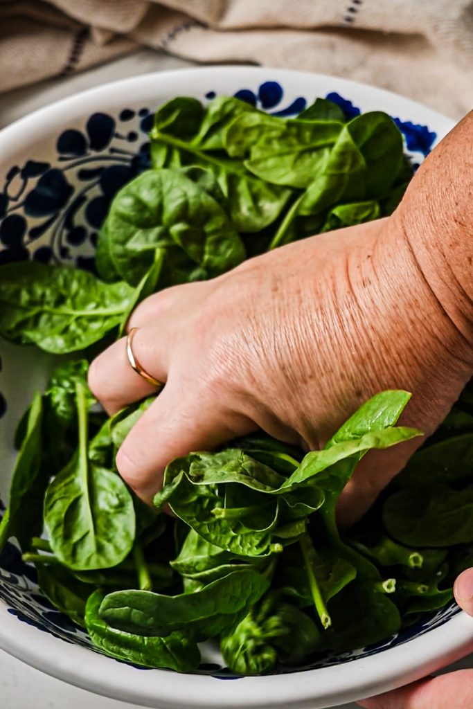 Hand massaging the spinach in a bowl.