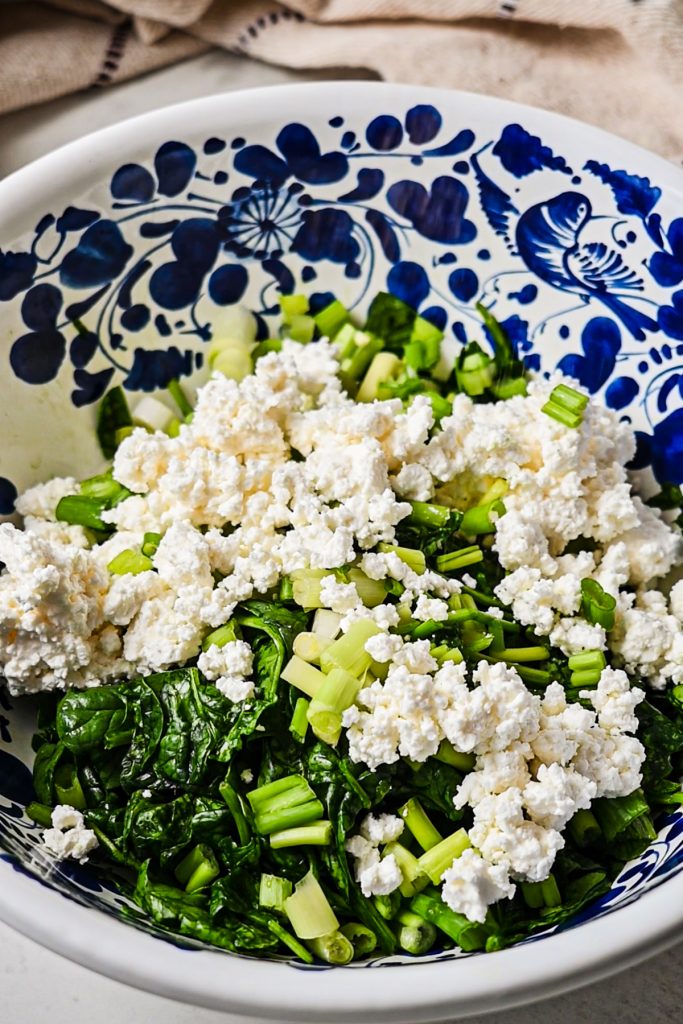 Crumbled feta cheese added to the mixing bowl with spinach and scallions.