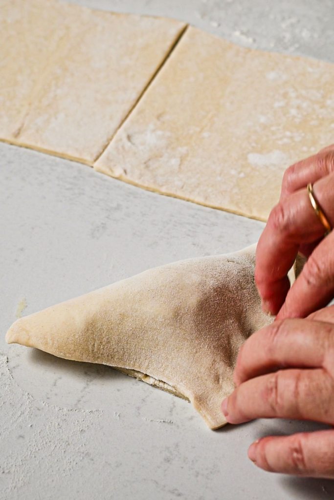Hand assembling the spanakopita turnover by folding the puff pastry over the filling.