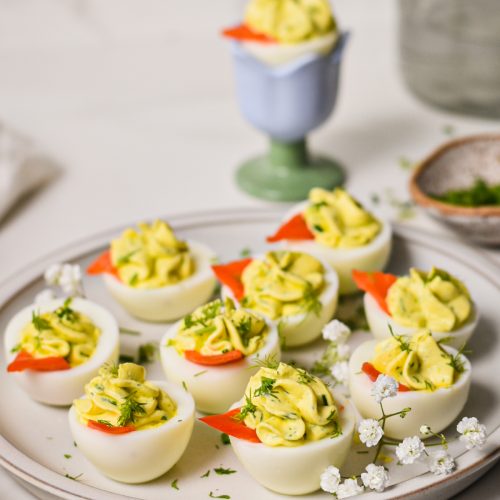 Deviled eggs garnished with smoked salmon and dill served on a white plate.