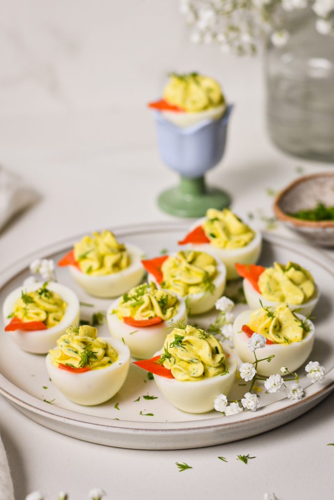 Deviled eggs garnished with smoked salmon and dill served on a white plate.