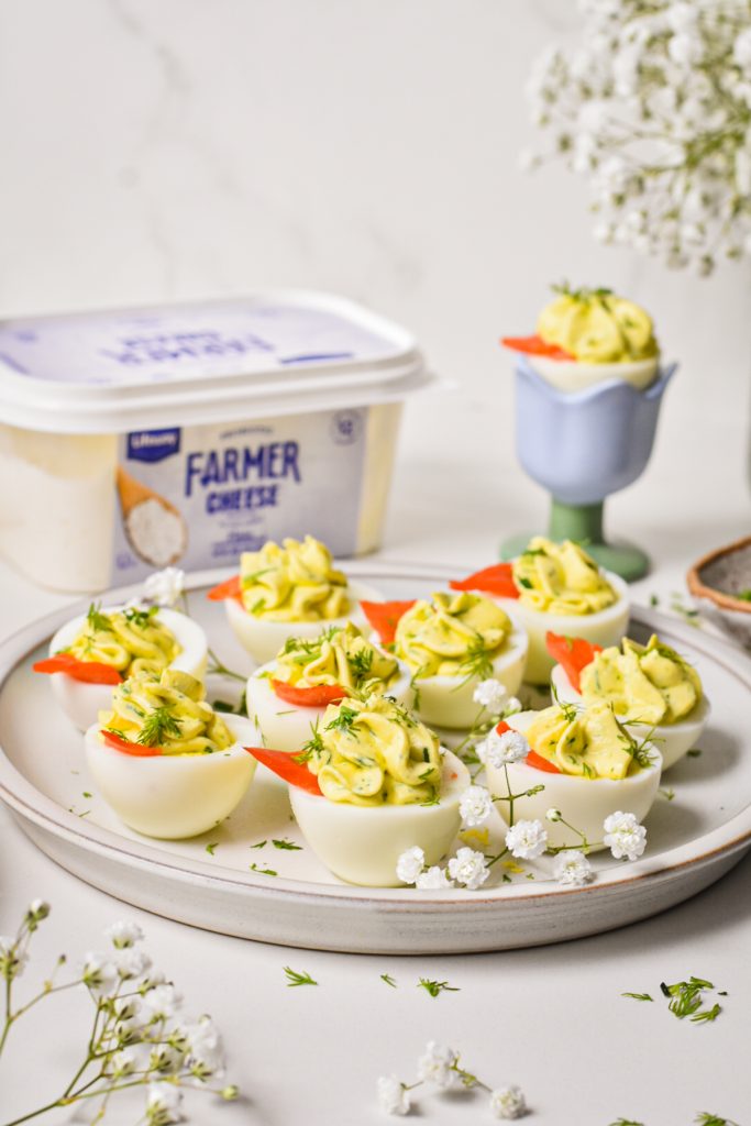Deviled eggs served on a serving plate with a tub of farmer cheese in the background.