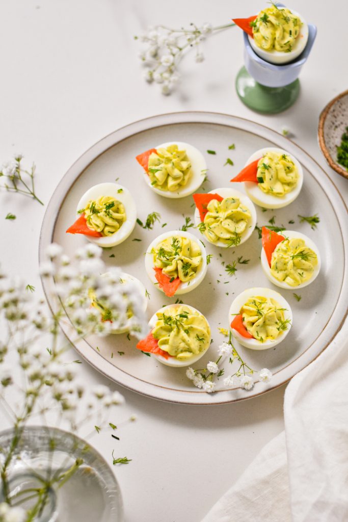 Overhead shot of deviled eggs on a serving plate garnished with smoked salmon and dill.