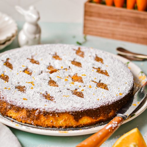 Carrot orange torta caprese on a serving plate with powdered sugar on top.