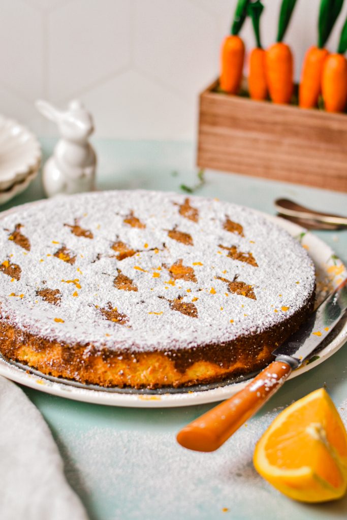 Carrot orange torta caprese on a serving plate with powdered sugar on top.
