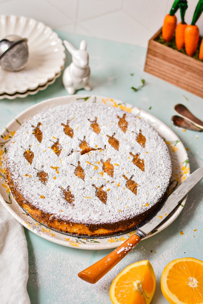 Carrot orange torta caprese on a serving plate with shapes of carrots on the top from powdered sugar.