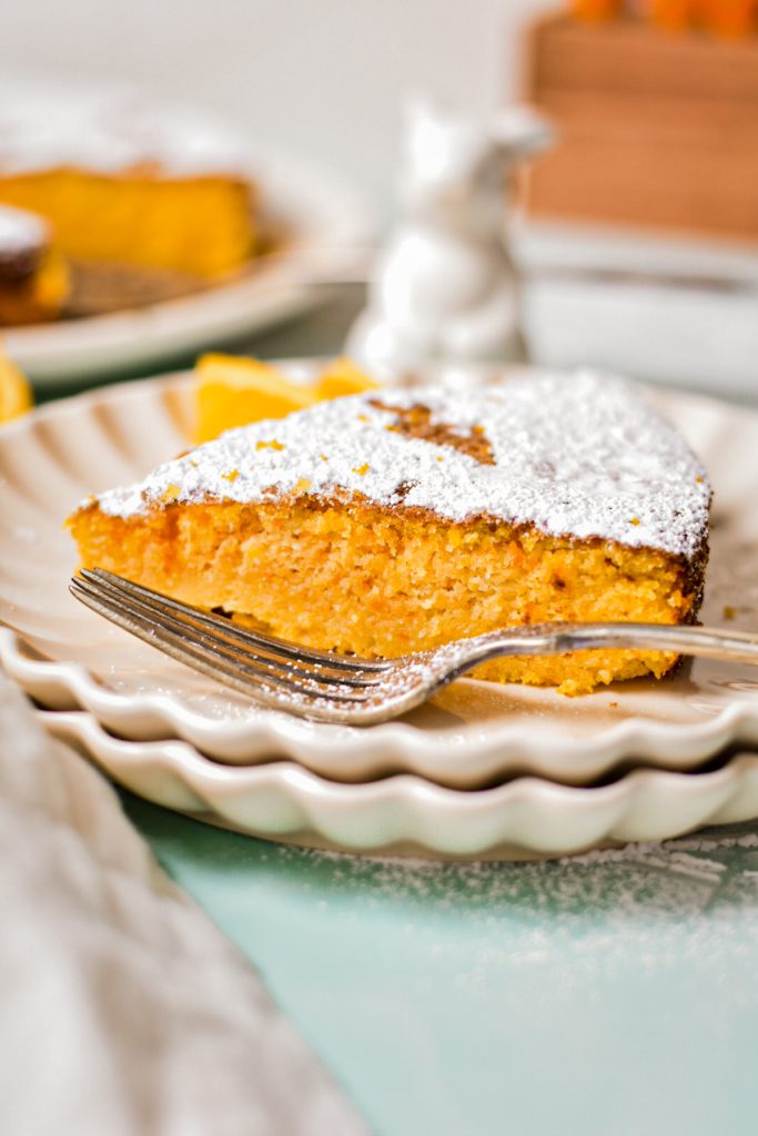 Slice of carrot orange torta caprese on a ruffled white plate with a fork.